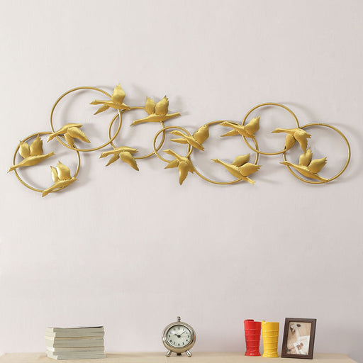 The metallic silhouette of this traditional wall decoration features a flock of birds flying in formation against an invisible wind current. Each gold bird is carefully crafted in iron and connected to the flock by a meandering iron circle frame that positions the avian flight pattern in place. An intriguing wall ornament over a fireplace or farmhouse-style headboard, the dynamic design of this decorative statue can be hung horizontally to visually expand the dimensions of your wall space.