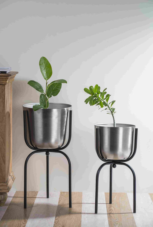 Bring a taste of the green outdoors into the comfort of your own home with just the addition of some fresh plants. Use this modern inspired pot planter to grow your favorite flower, cactus, herb and more. It features a geometric stand, that allows this piece to be placed on the ground next to a desk, fireplace, or seating arrangement. The planter itself is crafted from galvanized metal.